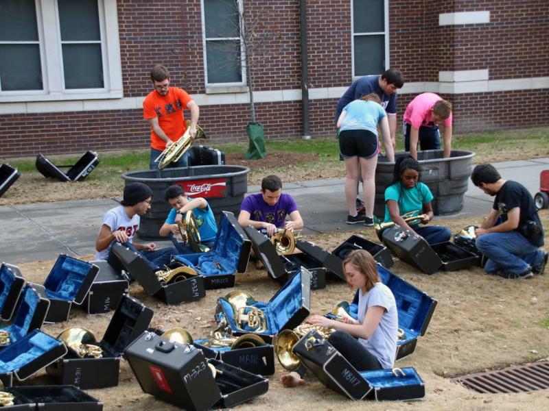 A group of students working on repairing brass instruments outside on the Couch building lawn.