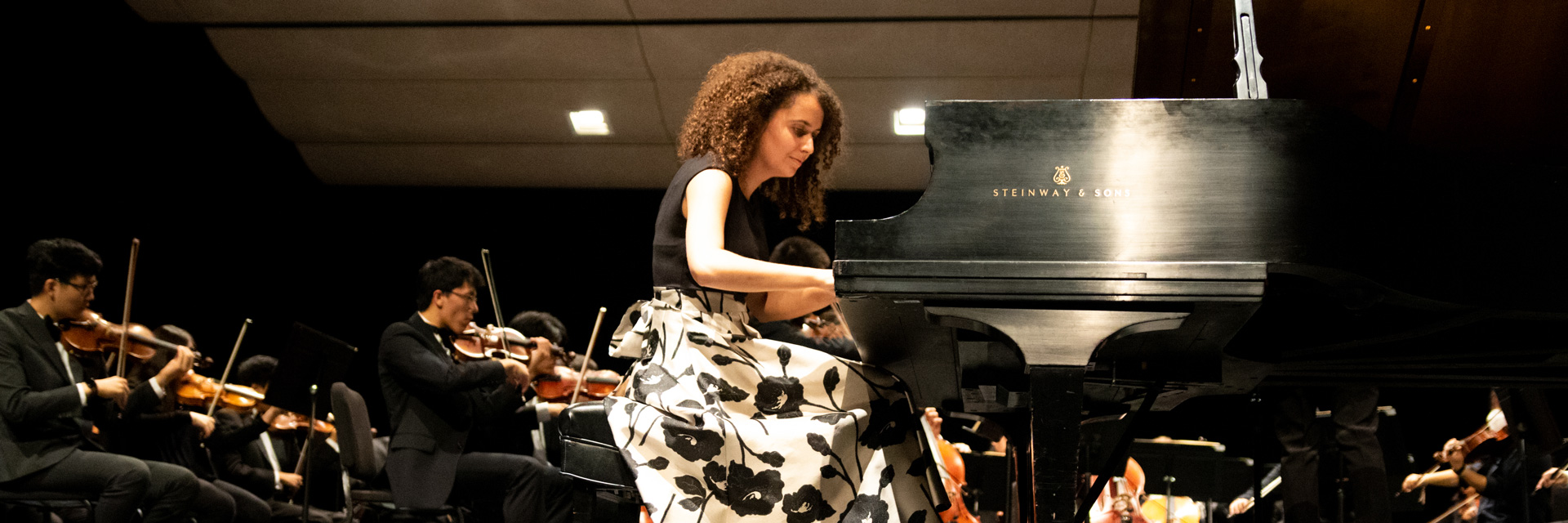 Laura Ballestrino playing grand piano in front of orchestra